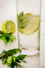 Cold fresh water with bubbles, lime, ice and mint in glass on white background