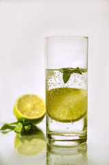 Cold fresh water with bubbles, lime, ice and mint in glass on white background