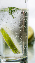 Cold fresh water with bubbles, lime, ice and mint in glass on white background