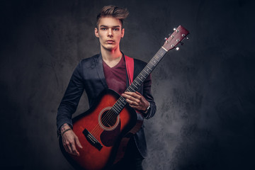 Obraz premium Stylish young musician with stylish hair in elegant clothes, playing on an acoustic guitar.