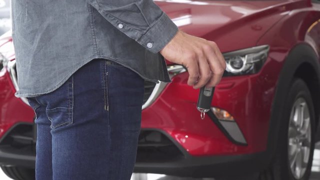Cropped shot of a male driver ready to open his car with a key. Man holding car keys standing in front of the automobile. Ownership, transportation, automotive industry concept.