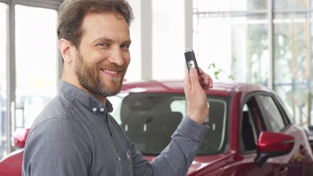 Mature bearded handsome man smiling posing in front of his new automobile holding car keys. Happy male customer buying a new auto. Cheerful male driver holding car key. Ownership concept.