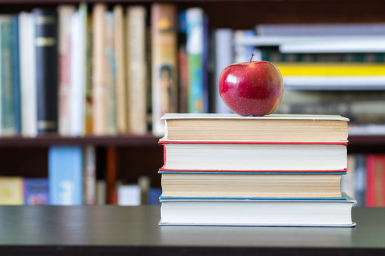 A stack of books with Apple on top on the background of bookshelves.