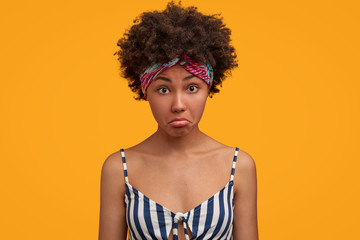 Pretty dark skinned female model looks in bewilderment, shocked to see something, wears casual sailor t shirt, isolated over yellow background. Lovely young African American housewife at home