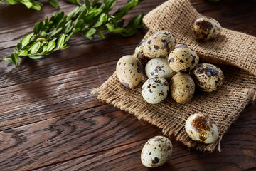 Quail eggs arranged in pyramid on a napkin with boxwood branches over a wooden table, close-up, selective focus.