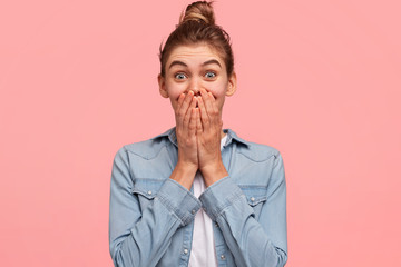 Young vivacious beautiful young female giggles joyfully, covers mouth, has fun alone, stands...
