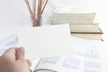 Education and business concept. A woman's hand hold a empty for text paper note on the open book with pile books and wooden pencil isolated on the white background.