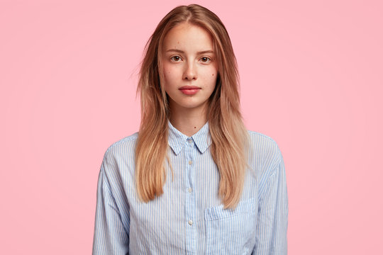 Photo of serious confident woman in formal shirt, has light hair and pleasant appearance, comes on business meeting, poses against pink background. Beautiful college student ready to pass exam
