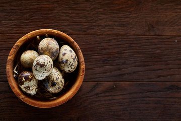 Obraz na płótnie Canvas Fresh quail eggs in a wooden bowl on a dark wooden background, top view, close-up