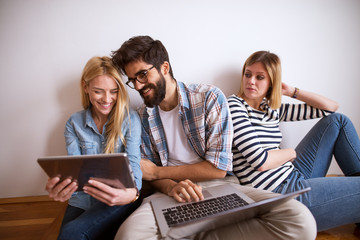 Two Young joyful stylish business sitting on the floor leaned against the wall while looking at...