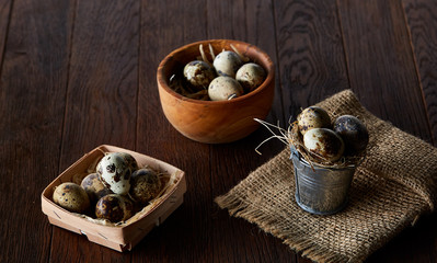 Rustic still life with quail eggs in bucket, box and bowl on a linen napkin over wooden background, selective focus