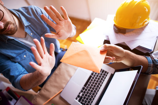 Young businessman is refusing a bribe in the envelope over the laptop from a contractor.