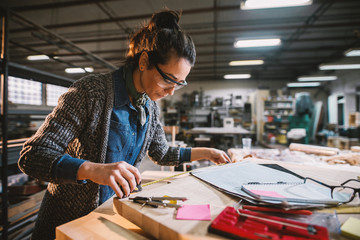 Thoughtful middle-aged industrial female engineer with eyeglasses working with a tape measure in the workshop.