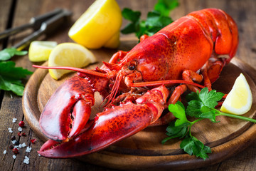 Steamed red lobster on a wooden cutting board with parsley and lemon - obrazy, fototapety, plakaty