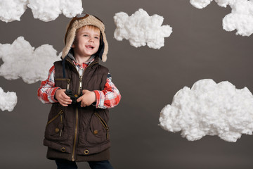 boy dressed as an airplane pilot stands between the clouds and looks through binoculars