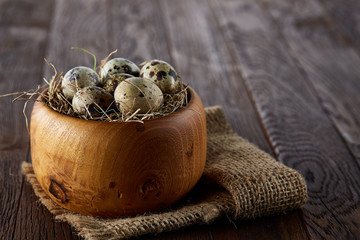 Fresh quail eggs in a wooden bowl on a homespun napkin over dark wooden background, top view, close-up