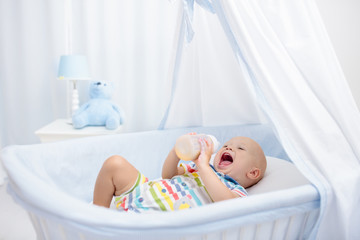 Baby drinking milk. Boy with formula bottle in bed
