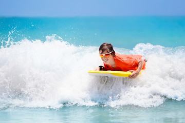 Child surfing on tropical beach. Surfer in ocean.