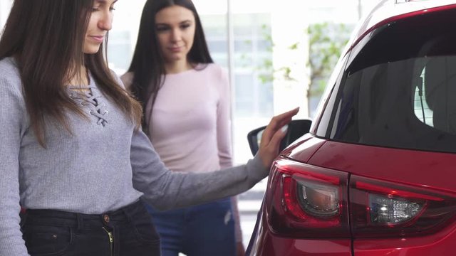 Cropped shot of a woman buying a new car at the dealership, choosing automobile with her best friend. Two female friends checking out new cars for sale. Retail, driving, transportation concept.