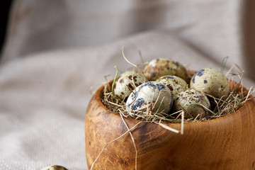 Quail eggs in a wooden bowl on a homespun tablecloth, top view, close-up