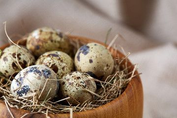 Quail eggs in a wooden bowl on a homespun tablecloth, top view, close-up
