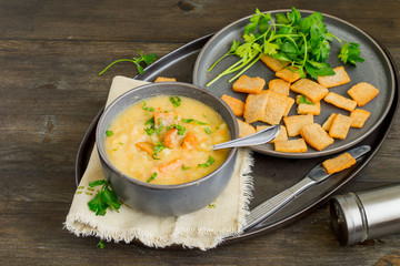 Pea thick soup in a bowl, next to fresh green parsley and small crispy croutons on a round dish. 