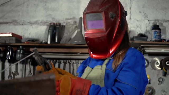 cute welder girl in uniform in the garage working with welding equipment. Women's work in art