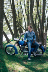 Fototapeta na wymiar Portrait young guy with sunglasses and Jeans jacket and pants posing sitting on his vintage retro motorbike. biker wearing jeans, fashion men. old timer age concept, 1960s style, vertical photo