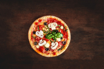 Fresh Pizza with  mushrooms, tomatoes, cheese and basil leaf  on wooden table closeup. Top view. Pizza Ready to Eat.
