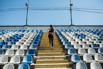 Naklejka premium Sporty girl in white shirt running fast on a stadium. Side view. Dynamic photo. Young woman in sportswear training on a stadium. Copy space. Sport lifestyle concept