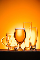 close up view of arranged empty glasses and mug of beer on orange background