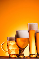 close up view of arranged mugs of cold beer with froth on orange background