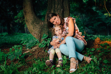 Mother with cute little daughter having fun sitting in the forest