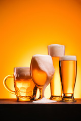 close up view of arranged mugs of cold beer with froth on orange background