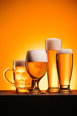 close up view of arranged mugs of cold beer with froth on orange background