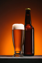 close up view of bottle and mug of beer on orange backdrop