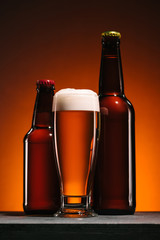 close up view of bottles and mug of beer with foam on orange backdrop