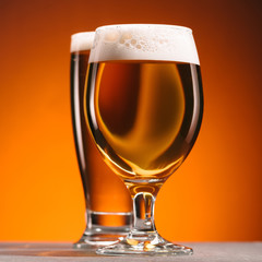 selective focus of arrangement of glasses of beer with froth on orange backdrop