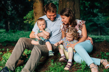 Young happy family of four sitting in the forest.