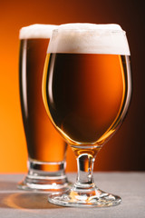 selective focus of arrangement of glasses of beer with froth on orange backdrop