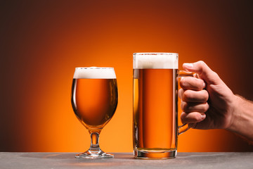 cropped shot of man holding mug of cold beer on orange background