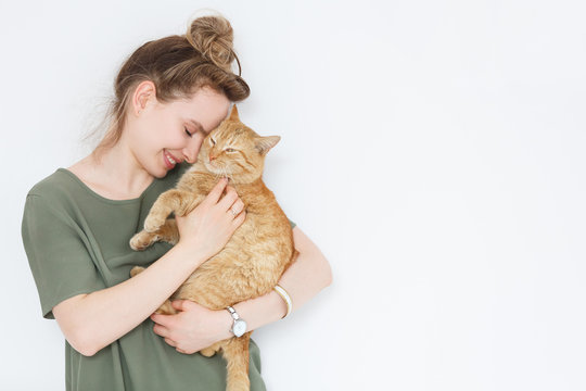 Closeup portrait handsome young hipster woman, hugs his good friend ginger cat on white wall background. Positive human emotions, facial expression, feelings. People and animals in love
