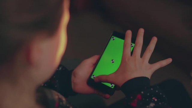 Little girl in dress uses her mobile phone with green screen. She moves her fingers across the screen.