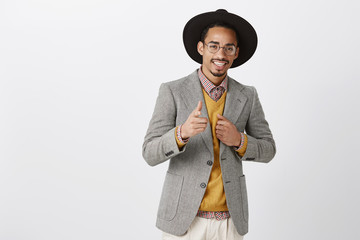 He can rely on you. Portrait of satisfied confident african-american guy in black hat and stylish jacket, showing gun sign at camera, boosting confidence near mirror before going out