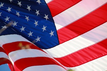 Close Up on American Flag Stars and Stripes Waving against Blue Sky Backlit by Afternoon Sun