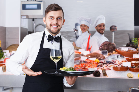 Portrait of positive waiter with serving tray offering dishes