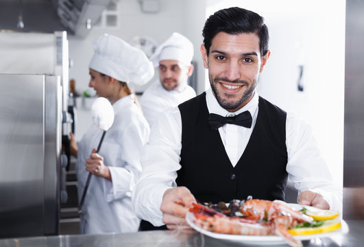 Waiter with dish of seafood in kitchen on restaurant