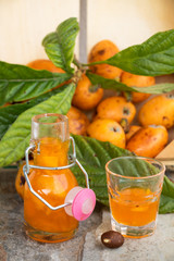 Ein Ast mit Früchten und Blättern der Mispel und ein Fläschchen Mispel Likör