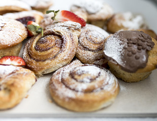 A selection of freshly baked and frosted Danish pastries and sweet buns on a business breakfast buffet sprinkled with icing sugar and garnished with strawberries in UK