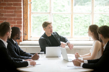 Male CEO pointing at watch reminding diverse subordinates group about meeting deadline, hurrying to finish work faster. Time is money. Concept of leadership, coworking and target date